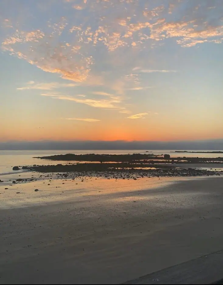 Sunset over a sandy beach and rocky low-tide waterline